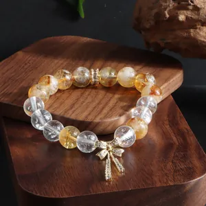 Nahaufnahme eines Naturkristall-Armbands mit funkelndem goldenem Schleifenanhänger