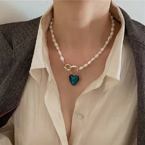 Modella indossa una collana di perle barocche con ciondolo a cuore blu e chiusura oro.