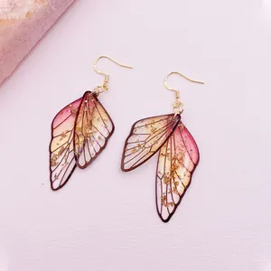 Macro view of handmade cicada wing earrings featuring pink gradient and gold foil flakes