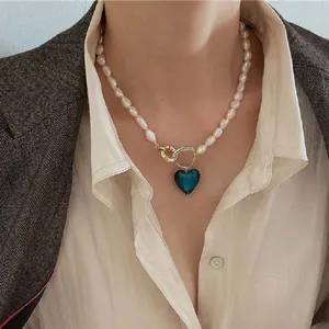 Primo piano di collana di perle barocche con ciondolo a cuore blu indossata con un blazer