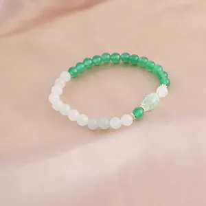 Detaillierte Nahaufnahme von elegantem grünen Achat- und weißen Kristallperlenarmband auf Seide