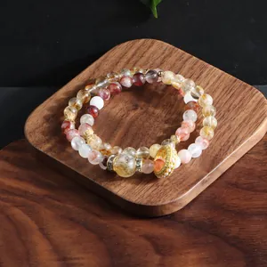 Detail shot of multi-layered natural crystal bead bracelet with golden charm on wood tray