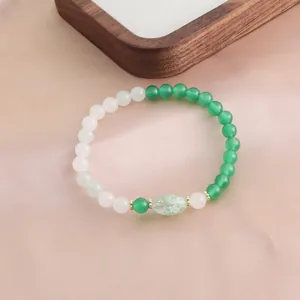 Nahaufnahme eines handgefertigten Armbands aus grünem Achat und weißem Quarz auf Satin.