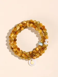 Macro view of double-layered golden tiger eye beaded bracelet with white shell charm