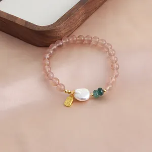 Detail view of pink strawberry quartz beaded bracelet with baroque pearl and golden Fu charm.