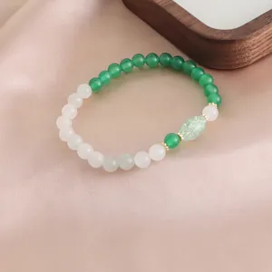 Detailansicht eines Armbands aus grünem Achat und weißem Kristall auf rosa Satin