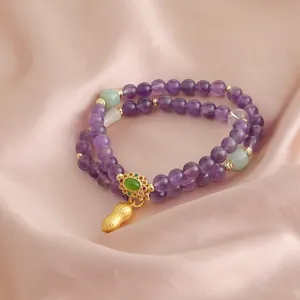 Primo piano di bracciale a doppio filo in ametista con ciondolo a forma di arachide d'oro