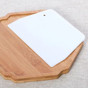 Close-up of white plastic trapezoid dough scraper tool on a wooden serving tray
