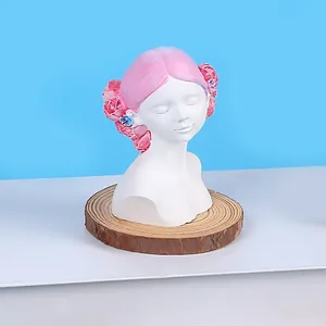 Close-up of a DIY girl bust candle featuring pink rose hair ornaments on a wooden base.