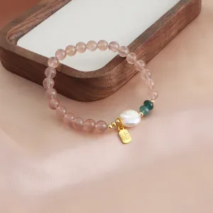 Macro view of a natural strawberry quartz bracelet with pearl and golden Fu charm