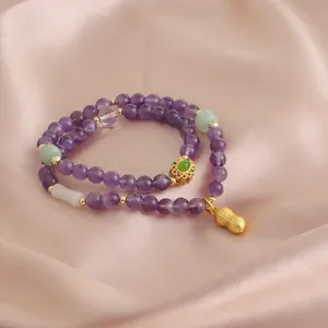 Dettaglio del braccialetto in ametista viola a doppio giro con ciondolo a arachide dorata.