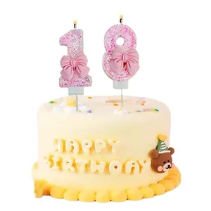Velas de cumpleaños número 18 con purpurina rosa y lazos decorativos en una tarta.