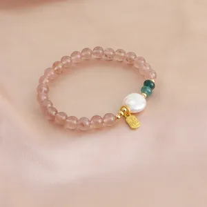 Close-up detail of natural strawberry quartz bracelet with white pearl and golden Fu charm