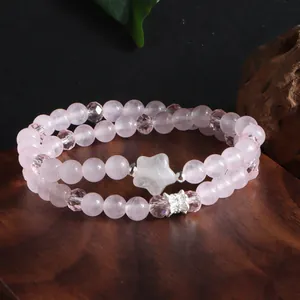 Bracelet double en quartz rose naturel avec perle étoile, présenté sur un socle en bois.