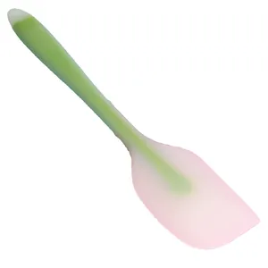 Integrated silicone baking spatula with pink head and green handle on white background