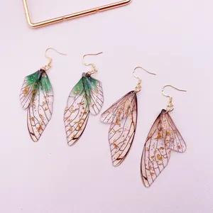 Macro detail of translucent cicada wing earrings featuring gold foil and glitter accents