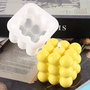 White silicone bubble cube mold shown with a finished yellow candle on a decorative magazine background