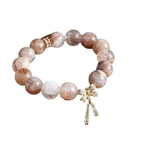 Elegantes Naturkristall-Perlenarmband mit einem funkelnden goldenen Schleifenanhänger