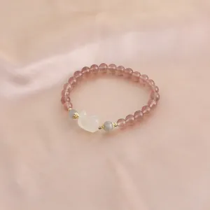 Close-up of a pink strawberry quartz bracelet with a cute white cat-shaped charm on silk.