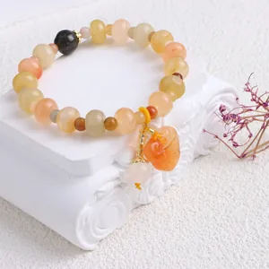 Nahaufnahme eines gelben Jadeperlenarmbands mit einem geschnitzten Flaschenkürbis-Anhänger.