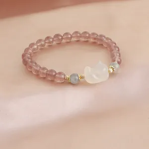 Macro detail view of a natural strawberry quartz bracelet featuring a white carved charm