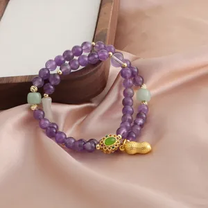 Dettaglio macro di un bracciale in ametista viola a doppio giro con ciondolo dorato