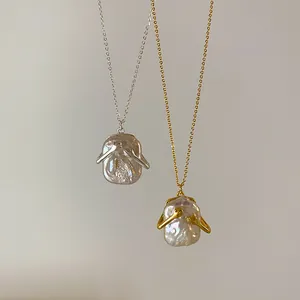 Macro dei ciondoli con perla barocca e mani che abbracciano in finitura oro e argento