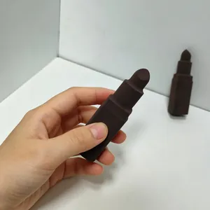 Primo piano di una mano che tiene una spugnetta per trucco marrone scuro a forma di rossetto.