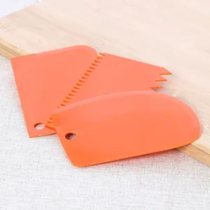 Three orange plastic dough scrapers with different edges on a wooden board
