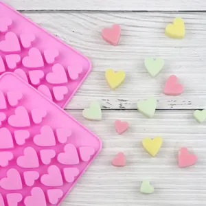 Heart-shaped pink silicone chocolate mold with colorful DIY candy hearts on wood
