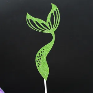 Macro view of a green glitter mermaid tail cake topper with elegant cutouts on stick.
