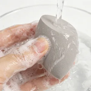 Close-up of a gray slanted makeup sponge being rinsed under water with soapy foam