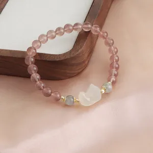 Close-up of natural strawberry quartz bracelet with white fox charm on satin background