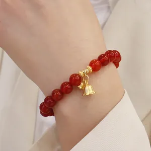 Nahaufnahme eines roten Achat-Perlenarmbands mit elegantem goldener Glockenanhänger.