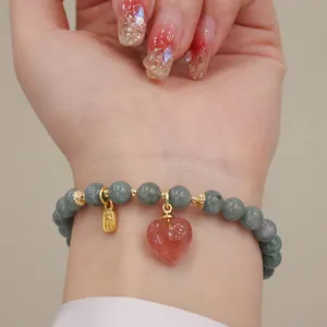 Dettaglio di bracciale in perline di giada con ciondolo a cuore in cristallo fragola al polso.