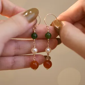 Primer plano de elegantes pendientes con cuentas de jade, perla y ágata naranja.