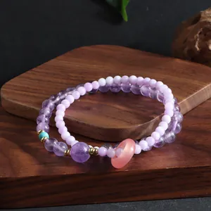 Detail view of double-layer amethyst beaded bracelet with pink donut charm on wooden base