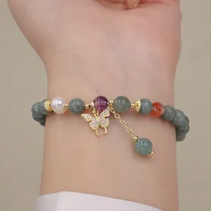 Dettaglio di un bracciale di perle di giada e cristallo con ciondolo a farfalla.
