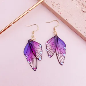 Detail of purple butterfly wing earrings with glitter and gold hooks on pink background.