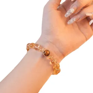 Gros plan d'un bracelet en citrine jaune avec une perle œil de tigre sur un poignet féminin.