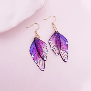 Close-up of purple gradient butterfly wing earrings with glitter and blue accents.