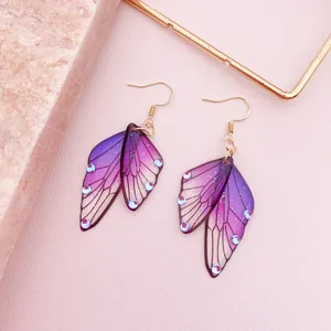 Macro detail of exquisite purple gradient cicada wing earrings with shiny glitter accents.