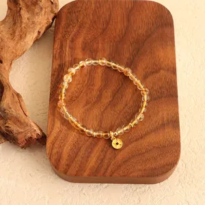 Nahaufnahme eines Citrin-Armbands mit einem Goldmünzen-Anhänger auf einem Holzbrett.