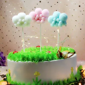 Detail of soft pom-pom cloud cake toppers in pink, blue, and green for birthday party.