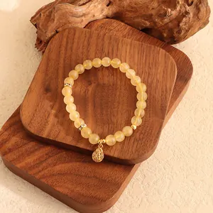 Detailansicht eines gelben Kristallarmbands mit einem goldenen Buddha-Anhänger auf Holz