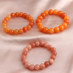 Detailaufnahme von drei Sonnenstein-Perlenarmbändern in Orange und Rosa auf Satin