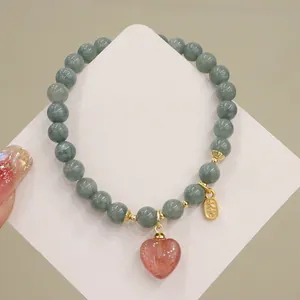 Dettaglio di un braccialetto in perle di giada con un ciondolo a cuore in quarzo fragola