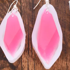 Gros plan de boucles d'oreilles en résine rose dans des moules en silicone.
