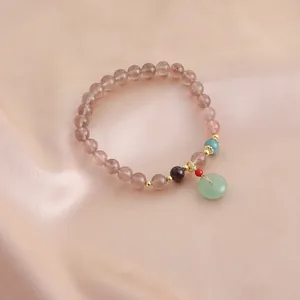 Close-up of a natural strawberry quartz bracelet with a green jade-style donut pendant on silk.