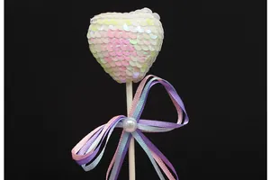 Close-up of iridescent sequin heart cake topper with colorful ribbon and pearl detail